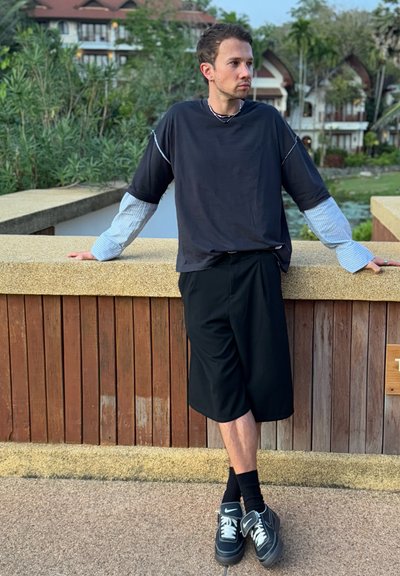 Camisa negra de manga corta con un patrón de rayas azules en las mangas, combinada con pantalones cortos negros y zapatillas negras. Estilo urbano casual.