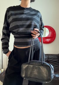 Haut à manches longues rayé noir et argent avec une taille cintrée, accompagné d'un petit sac à main en cuir noir avec fermeture éclair et double poignées.