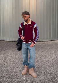 Vínový pletený sveter s béžovými a modrými pruhmi, svetlomodré džínsy a béžové masívne topánky. Čierna taška prehodená cez rameno, okuliare na tvári.