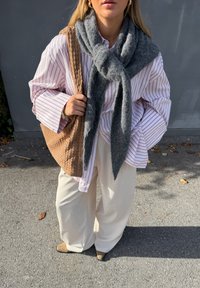 Stripete rosa og hvit oversized skjorte med vide ermer, grå ullskjerf, vevd tanfarget veske, kremfargede vide bukser og beige hæler.