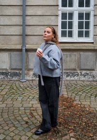 Pilkas trumpas švarkas su ilgais raiščiais, dėvimas ant juodų kelnių. Personažas laiko kavos puodelį, stovėdamas ant akmenimis grįsto tako šalia pastato.