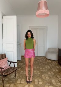 Haut vert sans manches, mini-jupe rose à sequins avec une fente sur le côté, assortie à des talons pointus imprimé léopard. Fond neutre avec parquet en bois.