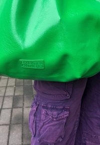 Πράσινη, γυαλιστερή τσάντα tote με υφή και ανάγλυφο λογότυπο "ESSENTIEL ANTWERP" σε ένα ορθογώνιο δερμάτινο πλακάκι.