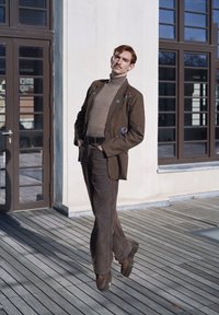 Chaqueta de traje de pana marrón con bordado floral, cuello alto beige y pantalones acampanados marrones a juego. El calzado tiene una suela gruesa y un tono oscuro.