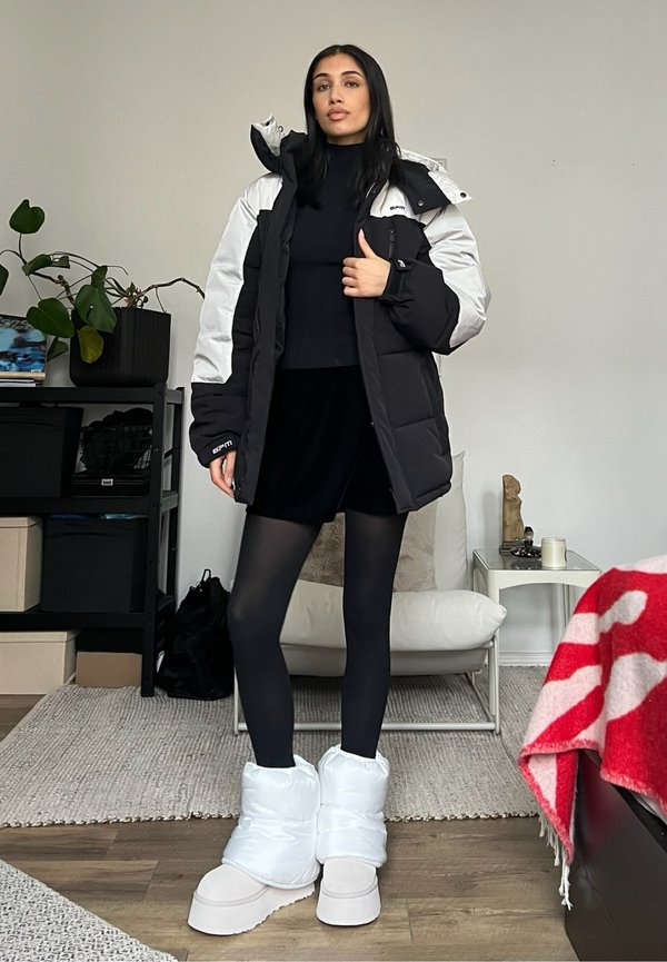 Chaqueta puffy en blanco y negro, top de punto texturizado, falda corta negra, medias negras, botas acolchadas blancas con suela gruesa, accesorios mínimos.