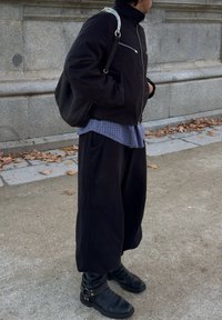 Μαύρο μπουφάν με φερμουάρ και ψηλό γιακά, τοποθετημένο πάνω από ένα μπλε καροτσάκι πουκάμισο. Χαλαρές μαύρες παντελόνες και μαύρες μπότες μέχρι τον αστράγαλο με λεπτομέρεια από λουράκι.