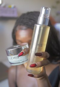 Due prodotti per la cura della pelle ELEMIS tenuti in una mano: una bottiglia spray in vetro smerigliato e un barattolo di crema leggera con un coperchio argentato lucido, entrambi etichettati.
