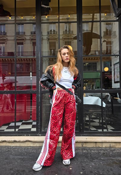 Pantalones de leopardo rojos con rayas laterales blancas, combinados con un top blanco corto y una chaqueta bomber negra. Zapatillas y un bolso pequeño.