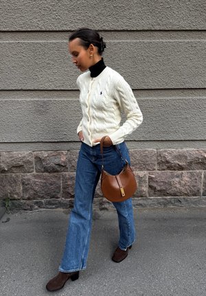 Cream cable-knit cardigan, black turtleneck, blue flared jeans, brown leather shoulder bag, and brown suede heeled boots. Textured background.