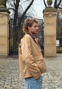 Veste légère beige avec col et poches avant, en tissu lisse. Portée sur une chemise marron, associée à un jean bleu délavé.