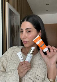 Drei Hautpflegeprodukte, die von einer Person gehalten werden: eine weiße Tube mit dem Aufdruck "Dr. Jart Ceramidin", eine silberne Flasche mit der Beschriftung "Good Genes" und eine orange Tube mit SPF.