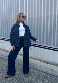 Τζάκετ από τζιν με κουμπιά μπροστά και δύο τσέπες στο στήθος, σε συνδυασμό με ψηλοκάβαλα, φαρδιά τζιν παντελόνια σε σκούρο χρώμα. Λευκό μπλουζάκι από μέσα.