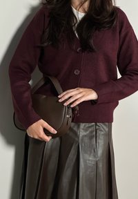 Μπορντό πλεκτό καρφωμένο μπουφάν με στρογγυλά κουμπιά, συνδυασμένο με καφέ δερμάτινη τσάντα και πλισέ σκούρα καφέ δερμάτινη φούστα.