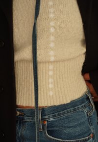 Maglione crema a coste con una finitura testurizzata e un dettaglio accentuato blu, abbinato a jeans di denim blu a vita alta.