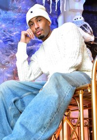 Chandail blanc en tricot torsadé, bonnet beige clair, jean bleu décontracté, assis sur une chaise dorée, avec un hibou des neiges et des accents de fond glacés.