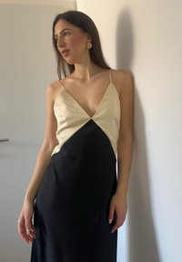 Sort og creme satin kjole med dyb V-hals, tynde skulderstropper og A-formet silhuet, der har et diagonalt farveblokdesign.