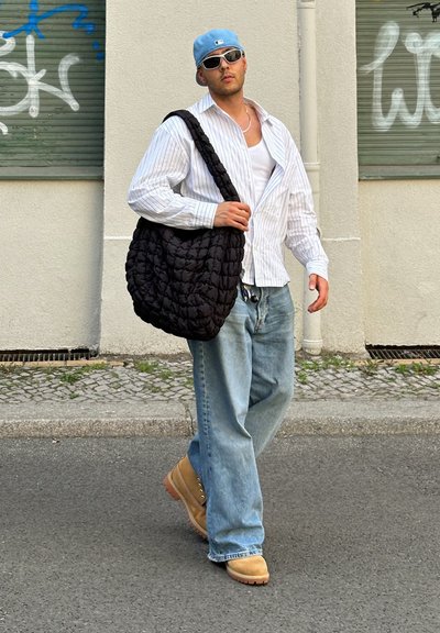 Bolso de hombro negro acolchado, camiseta de rayas blanca, top blanco, jeans azul claro y zuecos color beige, con una gorra azul clara y gafas de sol.