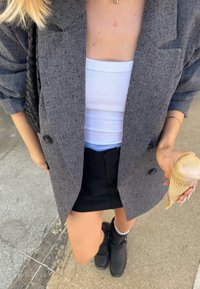 Blazer gris texturizado sobre una blusa blanca, combinado con una falda negra y botas negras de tobillo. Sosteniendo un cono de helado en una mano.