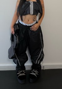 Top cropped preto e calças largas com riscas brancas, combinadas com botas pretas forradas a pele. Segurando uma bolsa em forma de guitarra preta.