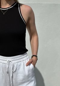 Čierny bezrukávový top s bielymi akcentmi, rebrovaná textúra. Skombinovaný s bielymi nohavicami na šnúrku, s voľným strihom a bočnými vreckami.