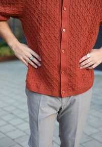 Rustfarvet strikket cardigan med et tekstureret diamantmønster, der har knapper foran og ribbet kant. Kombineret med lysegrå bukser.