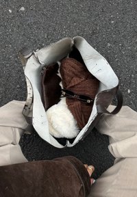 Stor brun lædertaske med tekstureret overflade, indeholdende en brun strikket genstand, en hvid pelsagtig genstand og sorte solbriller.