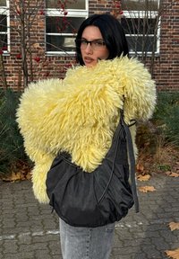 Gul fluffig texturerad kappa kombinerad med en svart läderväska. Väskan har en unik draperad design och bäraren har en avslappnad outfit.