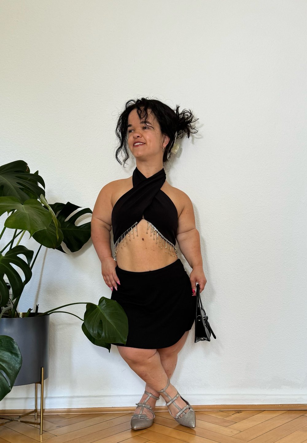 Top noir à col halter avec un design drapé et des franges argentées, associé à une jupe noire et des ballerines argentées. Un petit sac à main complète le look.