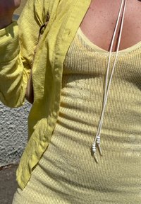 Luźny żółty len kardigan noszony na żółtej dzianinowej koszulce bez rękawów z wzorami kwiatowymi. Koszulka ma białe sznureczki z koralikowymi akcentami.