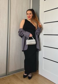 Ένα μαύρο φόρεμα με έναν ώμο σε στρώσεις με μια γκρίζα oversized σακάκι. Κρατά μια μικρή τσάντα από ασήμι με γκλίτερ και φορά μαύρες φλατ παπούτσια με διακοσμητικά.