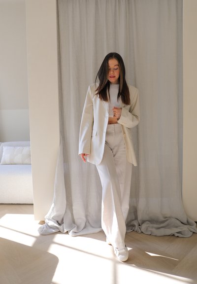 Blazer de lino beige sobre un top corto claro, combinado con pantalones a juego. El conjunto presenta un ajuste relajado y un diseño minimalista.