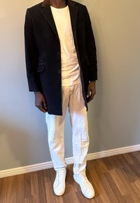 Manteau en velours côtelé bleu marine avec col marron, t-shirt blanc, pantalon léger en lin et baskets blanches sur fond uni.