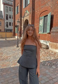 Μαύρη λινομένη μπλούζα με σχέδιο peplum και παντελόνι σε φαρδιά γραμμή. Το ύφασμα έχει λεία υφή και στο παρασκήνιο υπάρχουν πλακόστρωτοι δρόμοι.