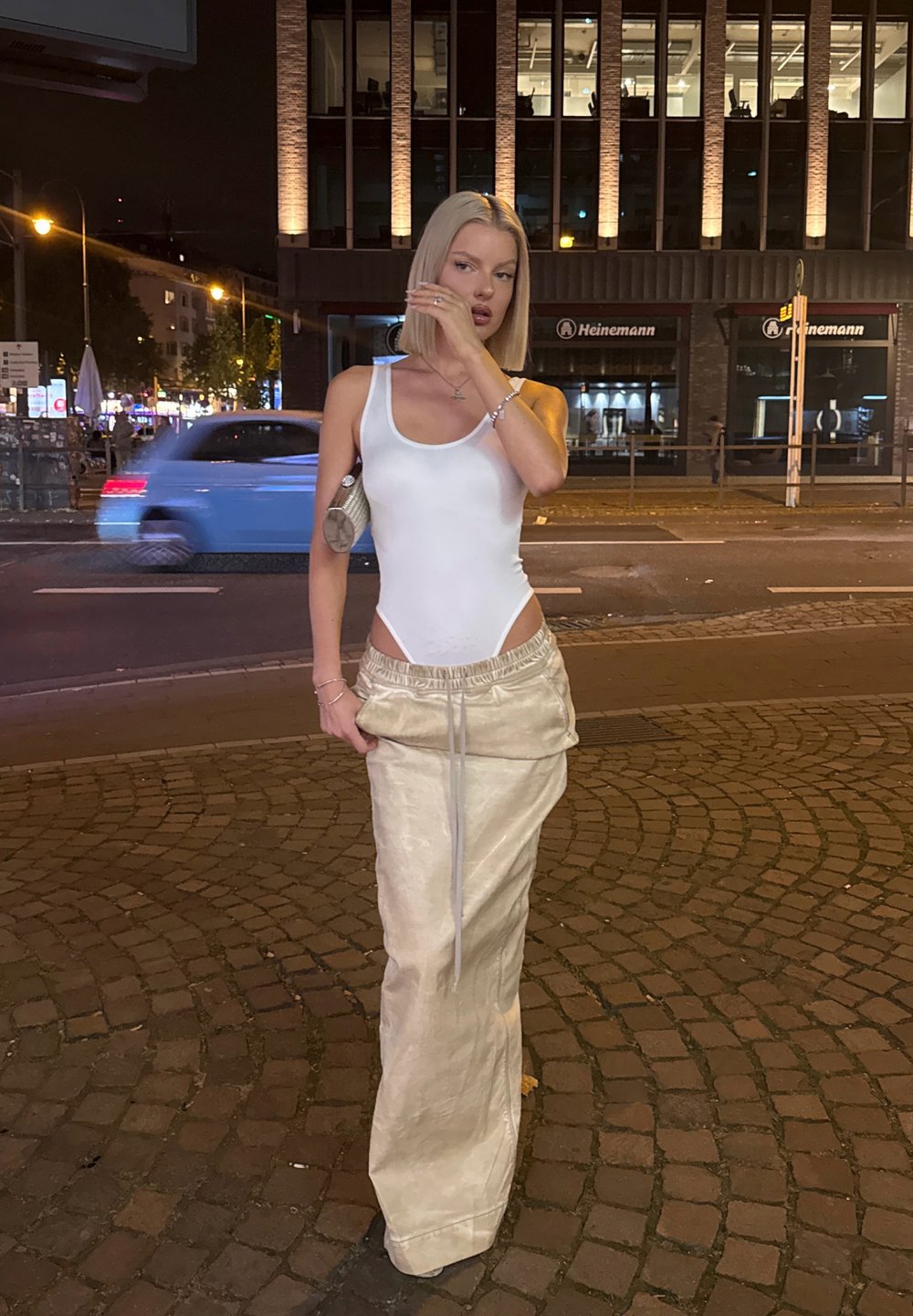 Konstruktsiooniga valge bodysuit külje lõigetega, kombineerituna kreemivärvi kõrge vöökohaga seelikuga, millel on nööriga vöökoht, linnakeskkonnas.