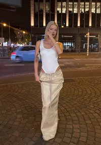 Konstruktsiooniga valge bodysuit külje lõigetega, kombineerituna kreemivärvi kõrge vöökohaga seelikuga, millel on nööriga vöökoht, linnakeskkonnas.