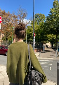 Olivově zelený oversized svetr s žebrovaným lemem, nošený s tmavě šedou sukní. Kožená taška s texturovaným povrchem a nastavitelným popruhem.