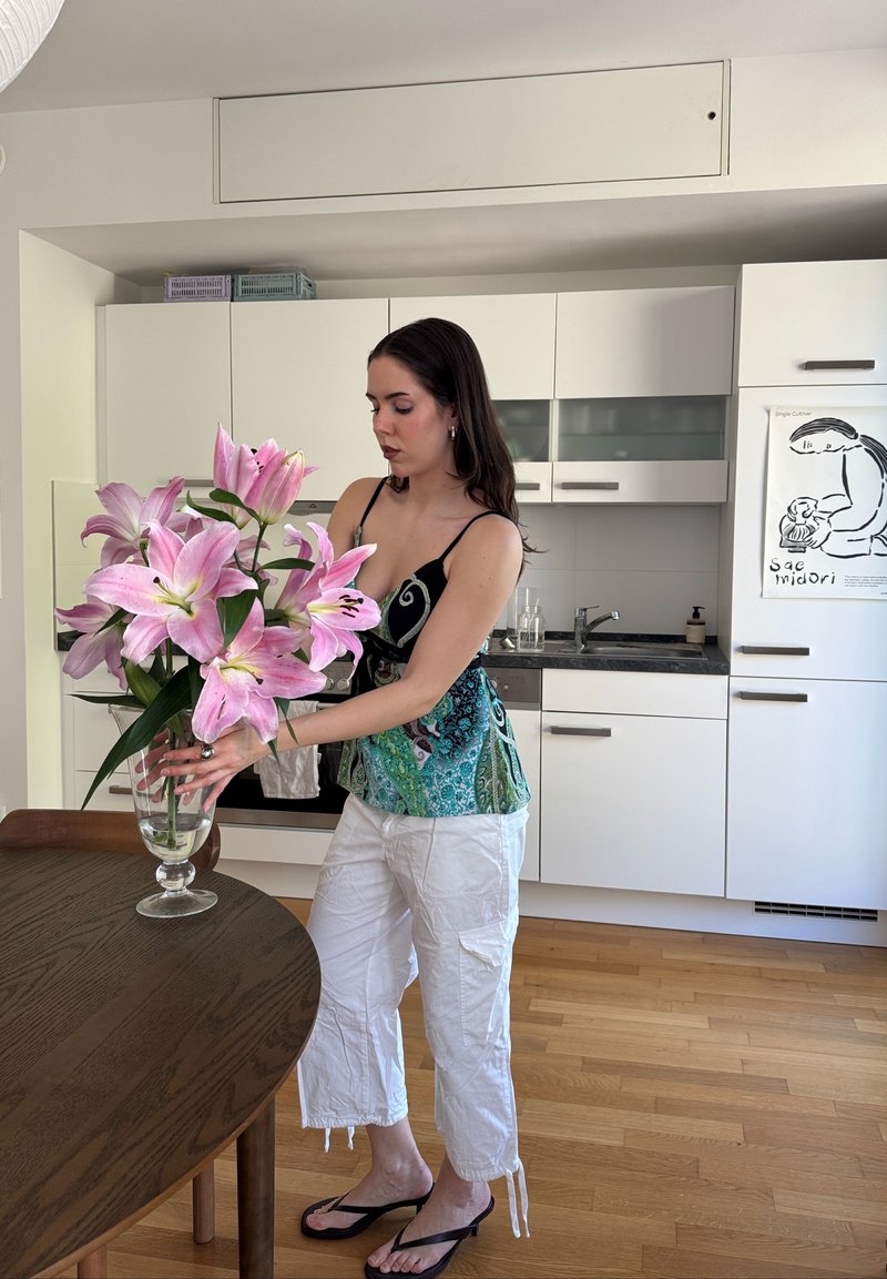 Nő nagy rózsaszín liliomokat rendez egy üveg vázában egy faasztalon egy modern, fehér konyhában.