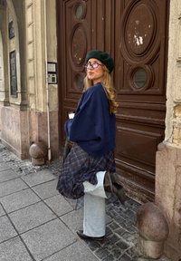 Marine oversized sweatshirt, ternet lagte nederdel, lyse denim jeans, sorte ankelstøvler, grøn beret, lilla briller, urban baggrund.