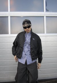 Czarna lekka kurtka na zamek z przodu, pod spodem kraciasta koszula, luźne ciemne dżinsy i we wzory bandana.