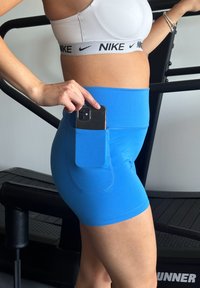 Shorts de sport bleus avec une poche latérale pour téléphone, fabriqués en tissu extensible, conçus pour le confort et la liberté de mouvement pendant les entraînements.
