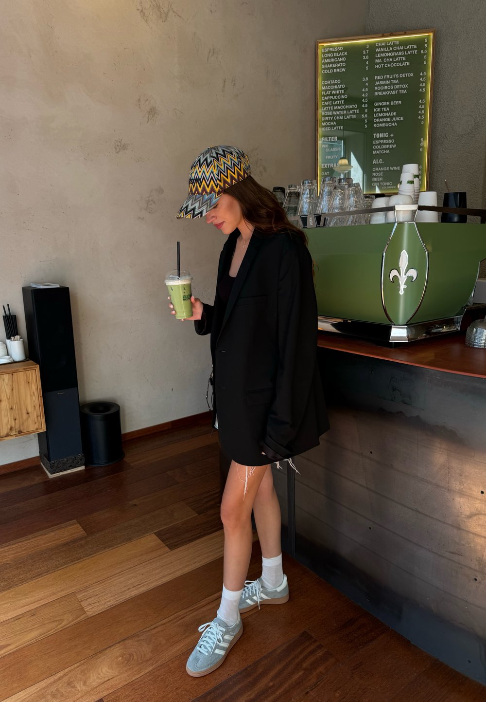 Blazer oversized preto, top preto, saia de ganga curta com bordas desfiadas. A usar um boné colorido com padrão zigzag e sapatilhas cinzentas com meias brancas.