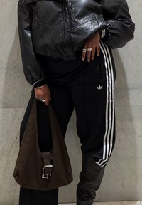Person iført sort læderjakke, sort Adidas træningsbukser med hvide striber, holder en mørkebrun taske med sølvspænde.
