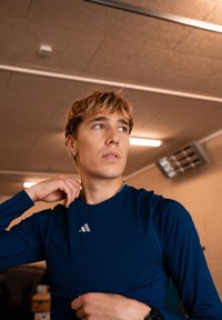 Soe pika varrukatega, keha külge liibuv sportlik särk tumesinisest siledast materjalist. Rinnal on väike valge Adidas'i logo.