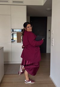 Burgundinen bleiseri samanvärís satin-hame, pörfá með marón NVIDIA skóm. Gleraugu og spjaldtölva fullkomna útlitið. Nútímaleg eldhúsumhverfi.