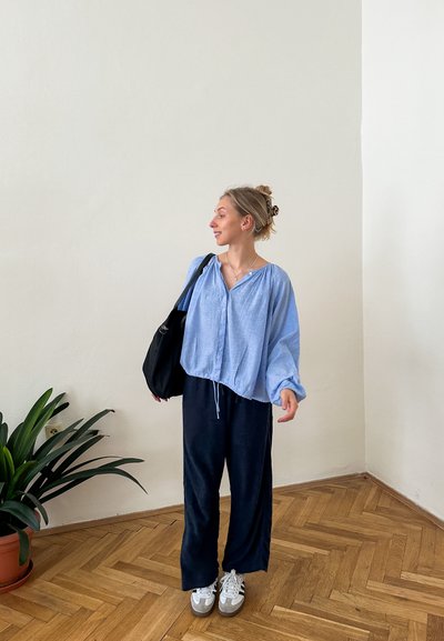 Blusa de lino azul claro con un dobladillo ajustable, combinada con pantalones oscuros de corte holgado en color negro. Un bolso negro y zapatillas blancas completan el conjunto.