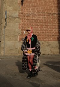 Maglione nero a maglia con applicazioni di orsi colorati, gonna rosa a strati, cappotto a fantasia, calze a rete e stivali neri robusti. Borsa argento.