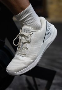 Hvit idrettssko med mesh-overdel, som viser et strømlinet design, teksturert finish og grå merkevareaccent nær hælen.