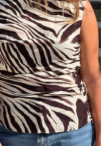 Zebramönstrad topp i mjukt tyg, med svarta och krämfärgade ränder, smockade sidor och rund halsringning, kombinerat med blå jeans.