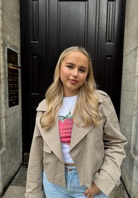 Beżowa krótka kurtka z klapami, noszona na białym t-shircie z nadrukiem czerwonej truskawki, w połączeniu z jasnoniebieskimi dżinsami.