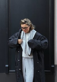 Fekete, oversize puffernadrág kabát patent gombokkal, alatta szürke kapucnis pulóver és hozzá illő szürke melegítőnadrág. Puha anyagok, laza szabás.